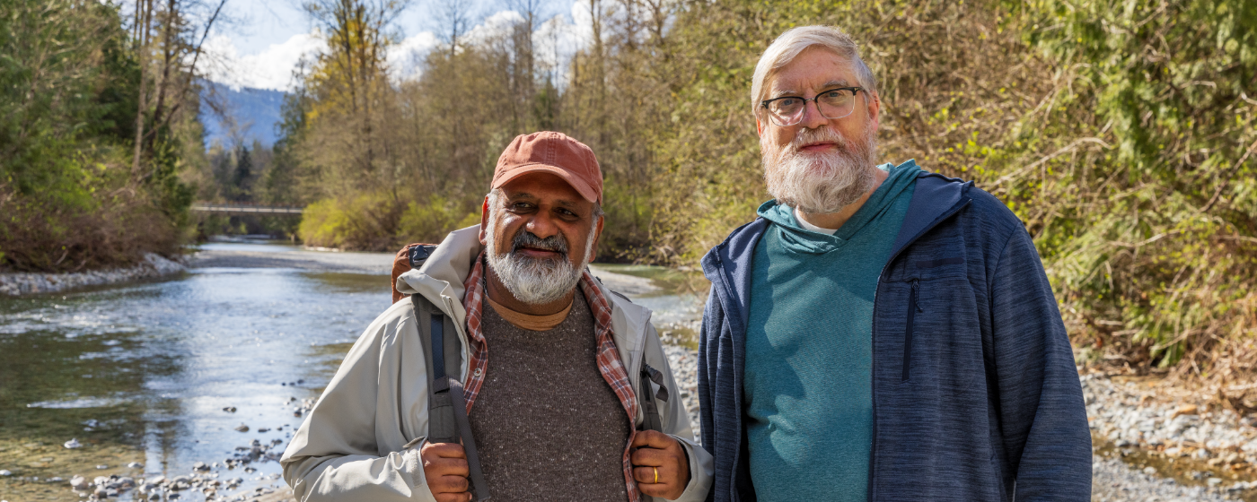 Two men pose in front of a creek before setting off on a hike